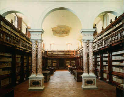 la sala monumentale della biblioteca statale di lucca è divisa in due da tre archi sorretti da colonne binate su piedistalli. le pareti perimentrali sono ricoperte di scafffali con libri