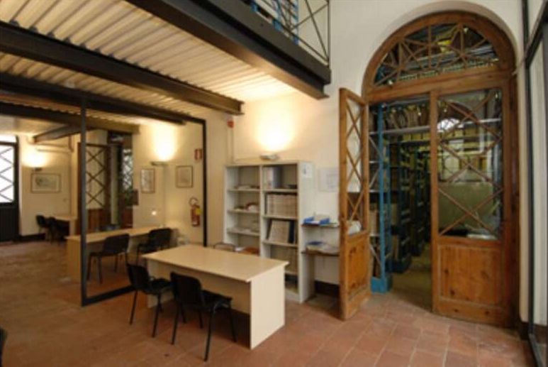interno dell'archivio comunale di Lucca. una sala luminosa con un tavolo e una porta in verto che si apre sulla sinistra.